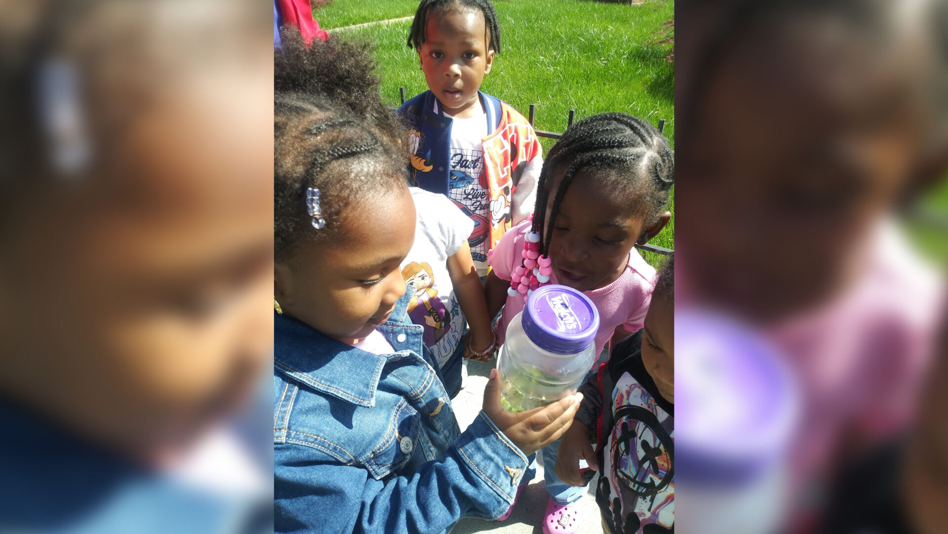 Children outdoors sharing a drink on a sunny day.