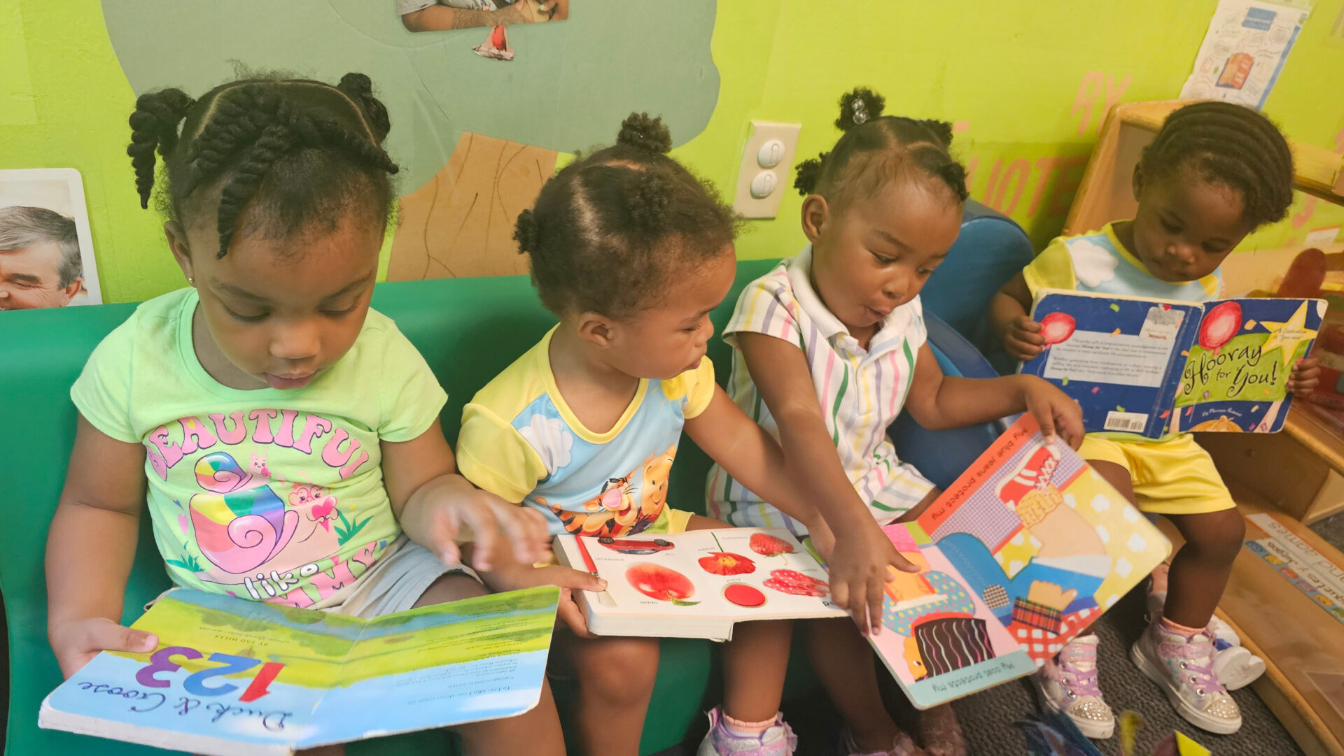Three young girls reading colorful books together in a cozy classroom.